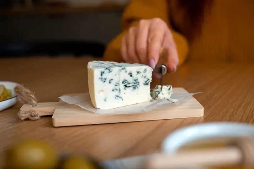 A woman cutting cheese over the chopping board and enjoying the rich, creamy blue cheese.